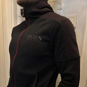Snygg svart/röd hoodie från Hugo Boss till salu. Knappt använd. Passar S och M.  