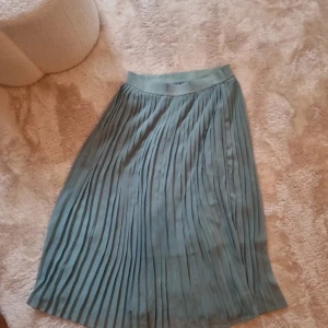 Grön plisserad kjol - En elegant grön plisserad kjol med elastisk midja. Kjolen har en mjuk och flödande design som ger en feminin och stilren look.