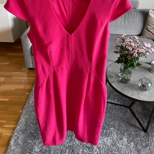 Vacker fuchsia klänning - En vacker rosa klänning med V-ringning och korta ärmar. Klänningen är figursydd och har en snygg passform. Perfekt för festliga tillfällen eller vardagligt bruk. Aldrig använd, bara tvättad. Kommer från rökfritt och djurfritt hem