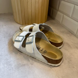 Birkenstock Arizona Narrow strl 38 - Storlek 38, 24,5 cm. Vita med mönster. Använt sporadiskt några veckor innan jag märkte att det vart alldeles för narrow för mig.   Skavanker i lädermönatret, normalt slitage. Sulor i fint skick. Ingen kartong kvar. Köpebevis finns
