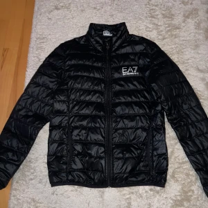 Emporio Armani EA7 Dunjacka Svart - Säljer Emporio Armani EA7 dunjacka där även en armani påse ingår. Storleken på jackan är S. Jackan är i mycket fint skick och har använt endast fåtal gånger. Bara och skriva för fler frågor eller bilder!