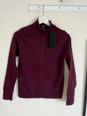 Aura seamless zip longsleeve från Relode  - Snygg vinröd träningsjacka från Relode med hel dragkedja framtill och hög krage. Tillverkad i ett stretchigt funktionsmaterial som passar perfekt till träning. Diskret logga på ryggen och långa ärmar med muddar. Aldrig använd, prislappen är kvar.  649 kr nypris 