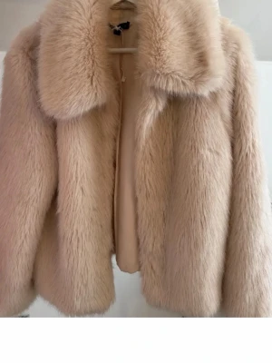 Beige fluffig pälsjacka - Säljer en supermjuk och fluffig beige pälsjacka med bred krage och rak passform. Jackan har en lyxig känsla och är perfekt för kalla dagar. Materialet är fuskpäls som ger en trendig look och den stängs framtill. Passar dig som vill ha en varm och snygg vinterjacka.
