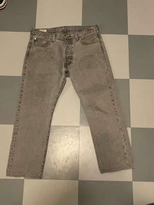  Levi's 501 gråa - Säljer ett par grå raka jeans från Levi's med klassisk femficksdesign och läderpatch bak i midjan. Jeansen har en vintagekänsla och är tillverkade i slitstark bomull. Perfekta för en avslappnad och trendig look.