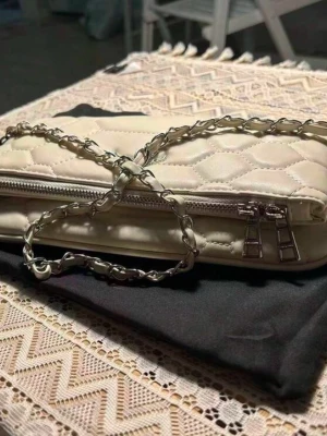 Handväska från Zadig & Voltaire  - En handväska från Zadig&Voltaire !!                            Snygg vit kuvertväska med quiltat mönster och silverfärgad kedjerem. Väskan har dubbla dragkedjor och är tillverkad i ett glansigt material som ger en lyxig känsla. Perfekt att bära över axeln eller i handen för en trendig look.