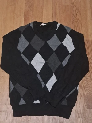 Svart och grå Meroan tröja - Säljer tröja i 100% bomull från Merona med klassiskt argylemönster i svart, mörkgrått och ljusgrått. Tröjan har rund halsringning och långa ärmar. 
