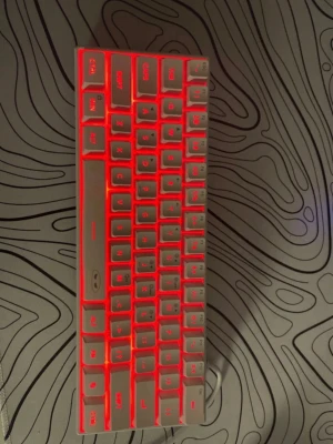 Kompakt tangentbord med röd belysning - Säljer ett kompakt mekaniskt tangentbord i vit plast med röd bakgrundsbelysning. Tangentbordet har en minimalistisk design och ansluts med kabel. Perfekt för gaming eller skrivbordssetup där du vill spara plats.