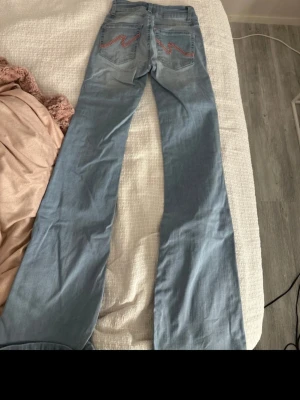 Ljusblå bootcut jeans med broderi från Nelly🥰 - Säljer ett par populära ljusblå bootcut jeans med snygga rosa broderier på bakfickorna från Nelly . Jeansen har utsvängda ben. Använda!🥰