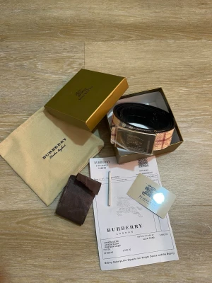  rutigt bälte med silverdetalj - Snyggt bälte  med klassiskt rutig design i beige och brunt. Bältet har ett stort silverfärgat spänne med ingraverad. Perfekt accessoar för att lyfta din outfit med en lyxig touch.