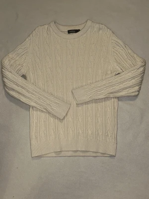 Beige kabelstickad tröja Dressmann XL - Snygg beige kabelstickad tröja från Dressmann i storlek XL. Tröjan har rund halsringning, ribbade muddar och nederkant samt ett klassiskt flätmönster. Perfekt för dig som gillar stilrena och tidlösa plagg. Använt bara 1 gång, helt ny skick
