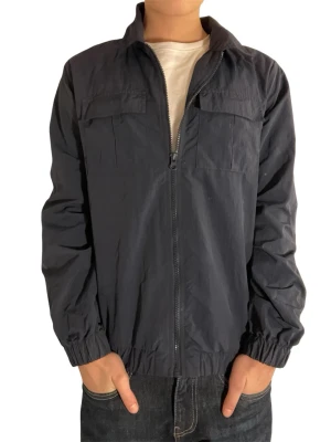 Mörkblå fealidjacka med dragkedja name it - Stilren Mörkblå vindjacka med hel dragkedja framtill, två bröstfickor och resår vid ärmslut och midja. Jackan har en klassisk krage och är tillverkad i ett lätt och smidigt material som passar perfekt för våren. Modellen är 167