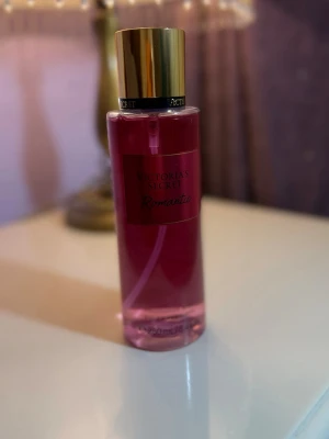 Victoria's Secret Romantic parfym - En snygg parfymflaska från Victoria's Secret i modellen Romantic. Flaskan är cylindrisk med rosa vätska och har ett elegant guldigt lock. Perfekt för dig som gillar fräscha och blommiga dofter.