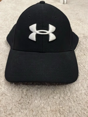 Svart keps från Under Armour - Säljer min keps från under armour i ny skick, har använts typ 2 gånger därför säljs den, passar nästan alla huvud storlekar men främst för yngre.