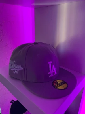 LA Dodgers grå New Era keps - Snygg grå keps från New Era med LA Dodgers-logga framtill och World Series-märke på sidan. Klassisk 59FIFTY-modell med platt skärm och broderade detaljer. Perfekt för dig som vill ha en sportig och trendig look.