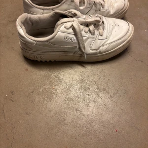Vita Fila sneakers i klassisk modell - Snygga vita sneakers från Fila med lågt skaft och klassisk siluett. Skorna har tydliga Fila-loggor på sidan och sulan, samt robust yttersula med mönster för bra grepp. Tillverkade i syntetmaterial och textil för en sportig look. Pris kan diskuteras vid snabb affär