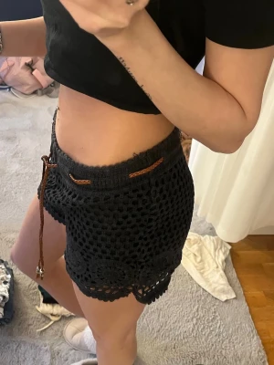 Svarta virkade shorts med snörning - Svarta virkade shorts med snyggt mönster och bruna snören i midjan.Perfekta för sommarens varma dagar.