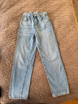 Ljusblå raka jeans med hög midja - Säljer ett par ljusblå jeans med rak passform och hög midja. Klassisk femficksmodell med knapp- och dragkedjegylf. Jeansen är i ett mjukt denimtyg och har en tidlös look som passar till det mesta.