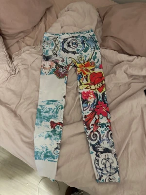Färgglada leggings med mönster - Säljer ett par unika leggings med färgstarkt och detaljerat tryck i blått, rött, gult och vitt. Mönstret har inslag av blommor, hjärtan och texten 'LOVE'. Tight passform och stretchigt material, perfekta för dig som vill sticka ut.