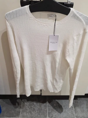 Vit ribbstickad tröja Stockh LM - Vit långärmad stickad tröja från Stockh LM Studio. Tröjan har en ribbstickad struktur och rund halsringning. Tunn och lätt i materialet, perfekt för lager-på-lager. Enkel och stilren design som passar till mycket.