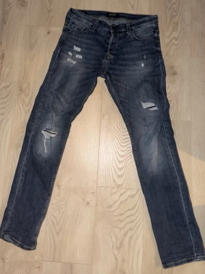 Slim fit jeans från Jack & Jones - Mörkblå slim fit jeans från Jack & Jones, modell Glenn. Jeansen har slitna detaljer och hål på benen för en trendig look. Klassisk femficksdesign och smal passform. Perfekta för dig som gillar en modern och avslappnad stil. 31/34 hör av dig vid frågor 