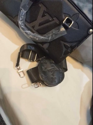 Svart Louis Vuitton handväska - Säljer en svart handväska från Louis Vuitton i präglat läder med det klassiska LV-monogrammet. Väskan har guldfärgade metalldetaljer, dubbla handtag och medföljande axelrem samt en liten rund coin pouch. Perfekt för dig som gillar lyxiga accessoarer.