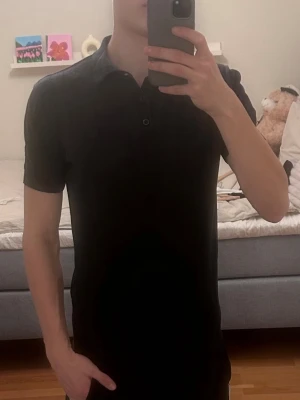 Svart pikétröja med krage - Klassisk svart pikétröja med krage och korta ärmar. Tröjan har knappar framtill vid halsen och en stilren, enkel design som skulle säga passar till det mesta. Hör gärna av vid intresse, priset är ej hugget i sten. MVH Erik