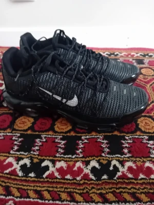Nike Air VaporMax Plus svarta sneakers - Nike Air VaporMax Plus sneakers i svart med reflekterande detaljer och tydlig Swoosh-logga på sidan. Ovandelen är i textil med mönstrad struktur och sulan har synliga luftbubblor för extra komfort. Snygg och modern design med sportig känsla.