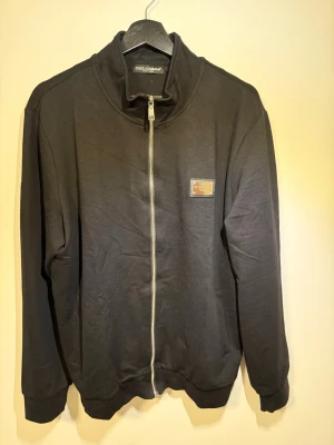 Dolce & Gabbana Kofta - Säljer en Dolce & Gabbana kofta. Använd en gång, skicket är som ny. Svart färg, silvrigt emblem. Hör av er vid frågor eller prisförslag.