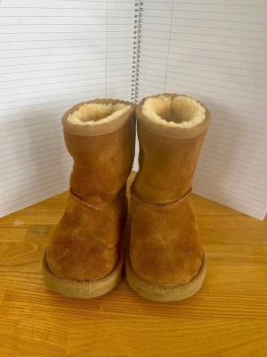 Bruna fårskinnsstövlar UGG - Säljer ett par original UGG Classic Mini barn i storlek EU 25. Klassiska och populära vinterskor med varmt ullfoder och bekväm passform. Perfekta för höst och vinter.  Skorna är hela och fullt fungerande, se bilder för egen bedömning. Kommer från rök- och djurfritt hem.  Märke: UGG Modell: Classic Mini Storlek: EU 25 Färg: Brun