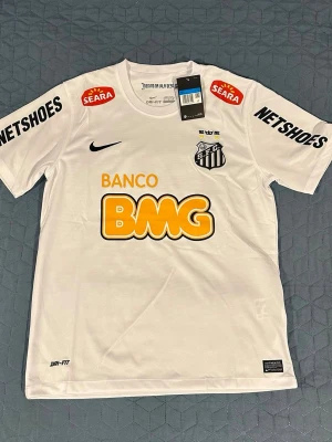 Neymar JR Santos fotbolls tröja  - Santos officiella fotbollströja i vitt från Nike med Neymar JR och nummer 11 på ryggen. Tröjan har flera sponsorloggor, rund hals och korta ärmar. Tillverkad i lätt och ventilerande Dri-FIT-material, perfekt för träning eller match.