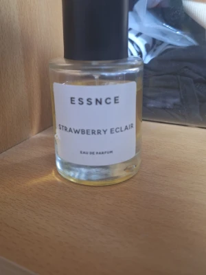 ESSNCE Strawberry Eclair parfym - Fräsch parfym från ESSNCE med doften Strawberry Eclair. Kommer i en rund, genomskinlig glasflaska med svart lock och vit etikett. Eau de Parfum med en söt och bärig karaktär, perfekt för dig som gillar fruktiga dofter.