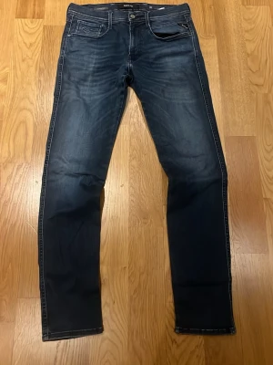Blå raka jeans från Replay W33 L34 - Snygga blå jeans från Replay med raka ben och klassisk femficksdesign. Jeansen har en lätt tvättad look med diskreta slitningar och kontrastsömmar. Perfekta för en avslappnad stil och tillverkade i mjukt denimtyg.