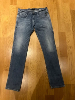 Blå slim fit jeans från Replay W34 L34 - Snygga blå slim fit jeans från Replay med klassisk femficksdesign och diskreta slitningar framtill. Jeansen har normal midja och dragkedja med knapp. Perfekta för en avslappnad och trendig look.