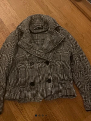 Rutigt skepparkavaj från ZARA - Stilren skepparkavaj från ZARA i svartvitt rutigt mönster. Dubbelknäppt med stora svarta knappar och bred krage. Kortare modell med klassisk skepparkavaj-look. Perfekt för dig som gillar tidlös och trendig stil.