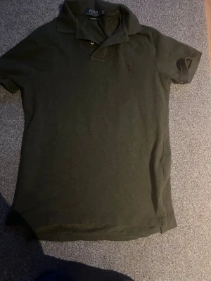 Mörkgrön piké från Polo Ralph Lauren - Snygg mörkgrön pikétröja från Polo Ralph Lauren med klassisk krage och två knappar vid halsen. Custom fit-modell med diskret broderad logga på bröstet. Perfekt till jeans eller shorts för en clean och stilren look.