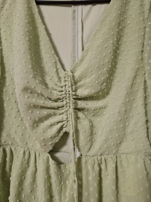Ljusgrön kortklänning från FB Sister - Supersöt ljusgrön kortklänning från FB Sister med v-ringning, långärmade ärmar och volangkant nertill. Klänningen har ett diskret prickigt mönster, snörning framtill och en liten cut-out under bysten. Perfekt för vår och sommar!