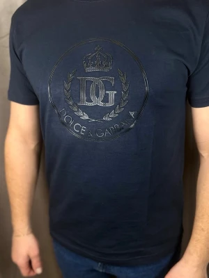 Mörkblå t-shirt från Dolce & Gabbana - Snygg mörkblå t-shirt från Dolce & Gabbana med ett stort, glansigt DG-logotyptryck och krona på bröstet. Klassisk passform och rund halsringning. Perfekt för dig som gillar exklusiva märken och stilrena detaljer.