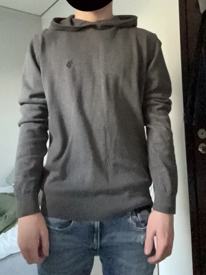 Mörkgrå hoodie från polo  - En stilren mörkgrå hoodie med huva och ribbade muddar vid ärmslut och nederkant. Hoodien har en diskret logga på bröstet och är tillverkad i ett mjukt material som känns skönt mot huden. Perfekt för dig som gillar en enkel och clean look. Saknas snören till den