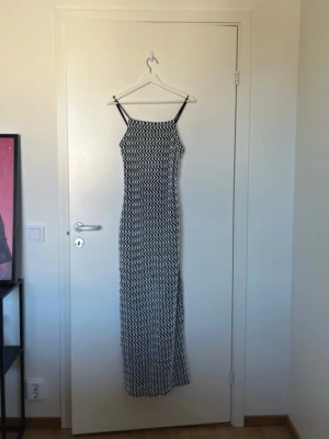 Svartvit långklänning med vågigt mönster - Säljer en svartvit långklänning med smala axelband och vågigt mönster. Klänningen har en rak passform och är ärmlös. Väldigt stretchigt material. Använd 1 gång på nyår. Nypris 899