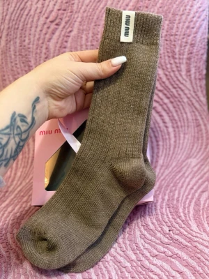 Bruna ribbade strumpor från Miu Miu - Snygga bruna ribbade strumpor från Miu Miu med en diskret logotyp på skaftet. Strumporna är i ett mjukt och stretchigt material som sitter skönt på foten. Perfekta för dig som vill ha en stilren och trendig look.