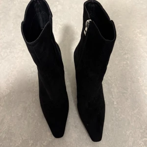 Svarta stövletter med transparent klack - Snygga svarta stövletter i mocka-look med spetsig tå och transparent hög klack. Dragkedja på sidan. Sparsamt använda, i mycket gott skick!