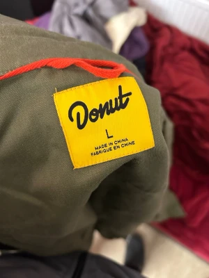 Grön skjorta från Donut i bomull - Snygg grön skjorta från Donut i storlek L. Skjortan har klassisk krage, knäppning framtill och en bröstficka med rödvit Donut-logga. Tillverkad i bomull och har långa ärmar. Perfekt för en avslappnad och cool stil.