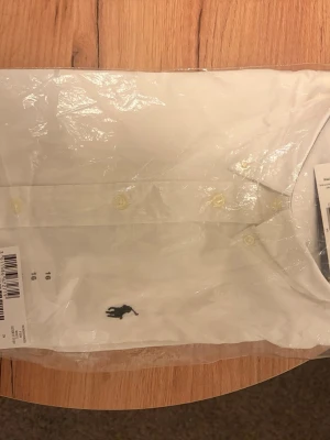 Vit skjorta från Ralph Lauren - Klassisk vit skjorta från Ralph Lauren med knappar framtill och broderad logga i svart på bröstet. Skjortan har en tidlös design och passar perfekt till många olika stilar. Tillverkad i bomull för en bekväm känsla.