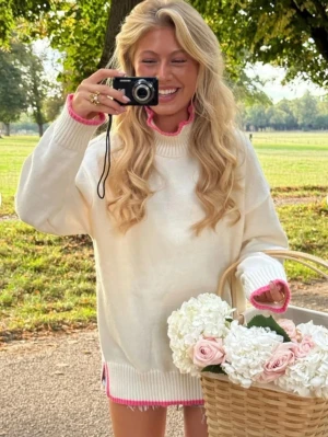 Vit stickad tröja med rosa detaljer - Superfin vit stickad tröja med ribbade muddar och snygga rosa detaljer vid hals, ärmslut och nederkant. Tröjan har en avslappnad passform och hög hals, perfekt för att hålla värmen under kyliga dagar. Passar perfekt till jeans eller kjol. Prislappen är tyvärr inte kvar men är 1 gång använd.