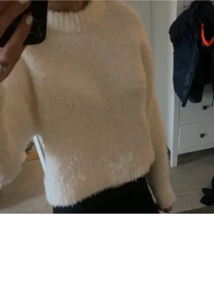 Vit fluffig stickad tröja H&M - Mysig vit stickad tröja från H&M med fluffig textur och rund halsringning. Tröjan har långa ärmar och en avslappnad passform som ger en chill vibe. Perfekt för kalla dagar när du vill vara både bekväm och snygg.