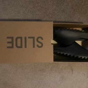 Adidas Yeezy Slide i svart, Onyx - 44.5 - Säljer ett par svarta Adidas Yeezy Slide med chunky sula och öppen tå. Knappt använda (4ggr) rengjorda efteråt.