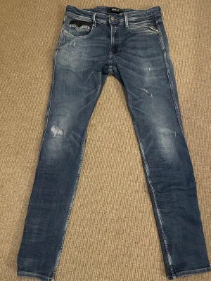 Replay Anbass slim jeans slitningar - Riktigt snygga slim fit replay jeans i modellen anbass och storleken W33/L34. Snygga slitningar och läderdetalj på fickan. Använd endast ett fåtal gånger och i mycket gott skick.