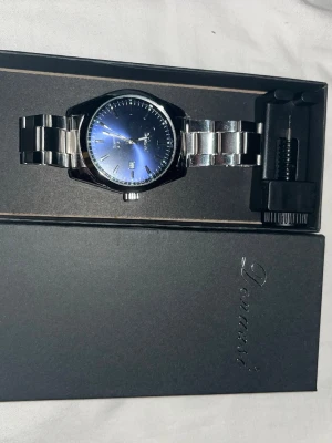 Devanti silverfärgad klocka blå urtavla - Stilren klocka från Devanti med silverfärgad länk i metall och en snygg blå urtavla. Klockan har datumvisning och klassisk design med tydliga indexmarkeringar. Perfekt accessoar för dig som gillar en modern och elegant look.