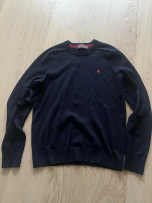 Mörkblå merinoullströja från Morris - Säljer en stilren mörkblå tröja från Morris i 100% merinoull. Klassisk rund halsringning och diskret röd logga broderad på bröstet. Perfekt till både jeans och chinos för en clean look.