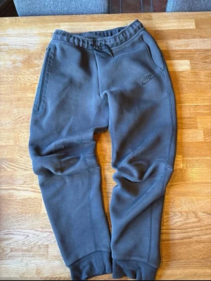 Gråa mjukisbyxor från Nike säljer bara på vinted - Snygga grå mjukisbyxor från Nike med diskret logga på låret. Byxorna har resår i midjan, muddar vid bensluten och praktiska sidofickor. Perfekta för chill eller träning, tillverkade i mjukt material som känns skönt mot huden.
